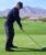 Man in dark clothing addressing golf ball on fairway with mountains and green landscape in background.